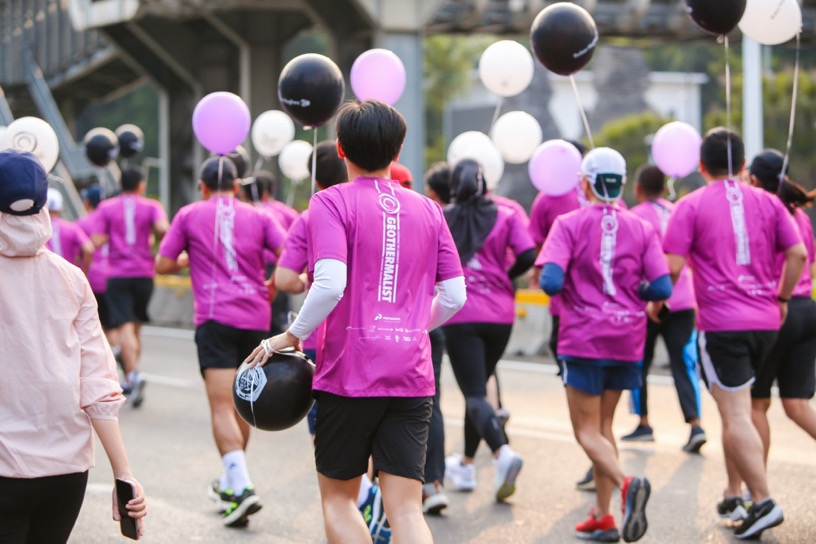 Runners in purple shirts carrying balloons along a city road.