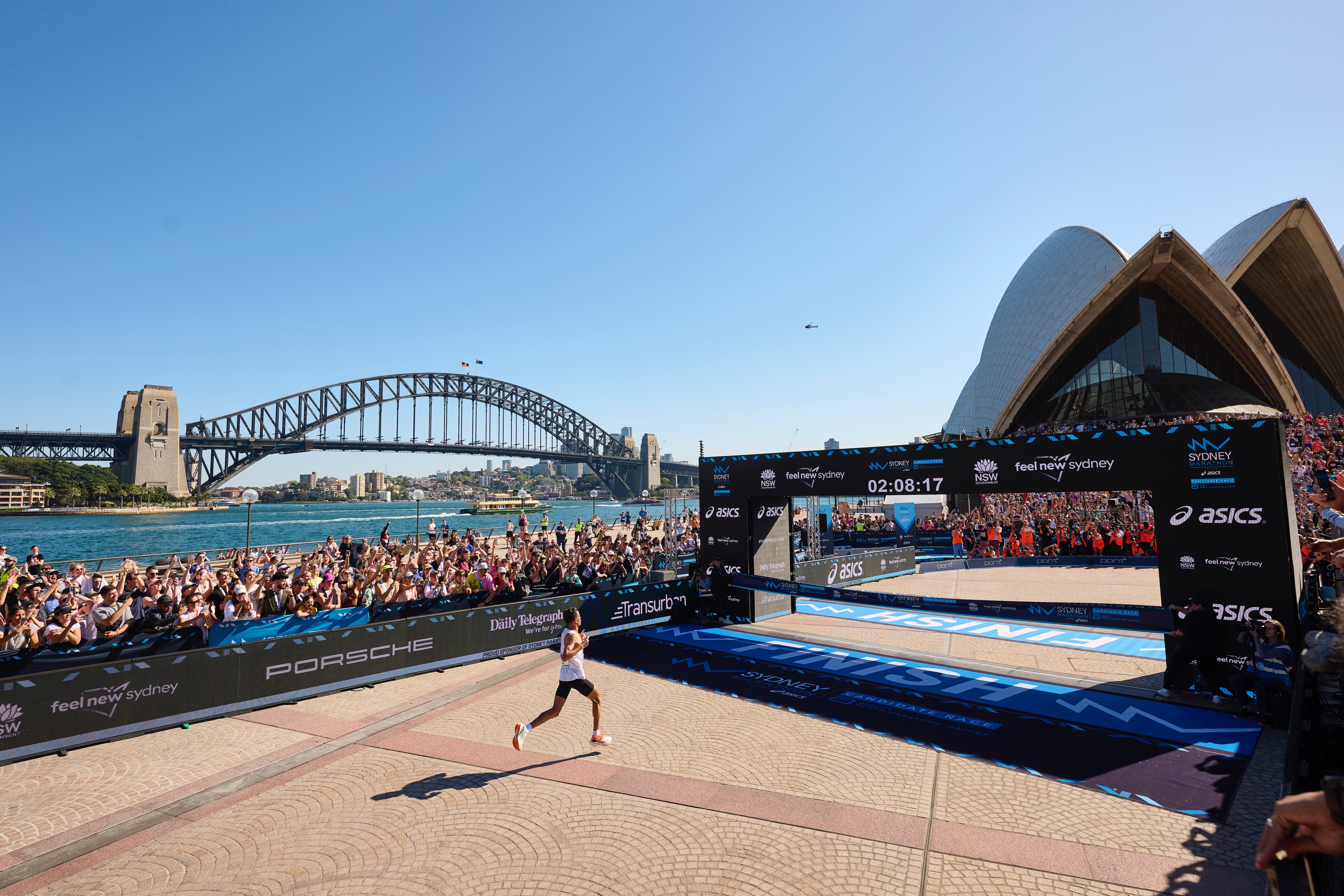 Runners on the Sydney Marathon course near the Opera House with race signage and spectators.